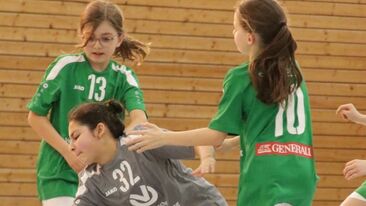 Spielszene im Jugendhandball: Zwei Spielerinnen im Zweikampf um den Ball in der Sporthalle, Nachwuchshandball im Vereinsbetrieb