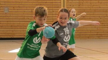 Zwei Kinder im Jugendhandball liefern sich einen Zweikampf um den Ball in der Sporthalle, dynamische Spielszene im Vereins-Nachwuchssport