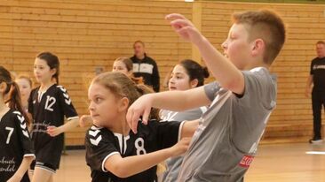 Zwei Kinder im Jugendhandball im Zweikampf um den Ball in der Sporthalle, intensive Spielsituation im Nachwuchs-Handballverein