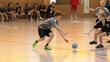 Kinder im Jugendhandball jagen dem Ball in der Sporthalle nach, dynamische Spielsituation im Nachwuchs-Handballverein